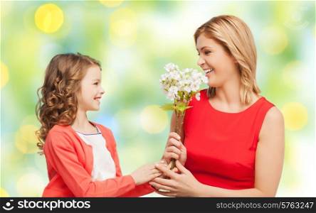 people, holidays, relations and family concept - happy little daughter giving flowers to her mother over green lights background