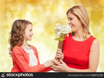 people, holidays, relations and family concept - happy little daughter giving flowers to her mother over yellow lights background