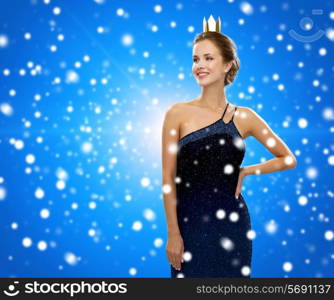 people, holidays, royalty and christmas concept - smiling woman in evening dress wearing golden crown over blue snowy background