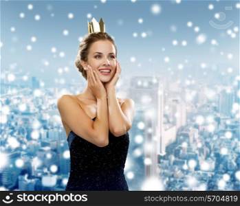 people, holidays, royalty and christmas concept - smiling woman in evening dress wearing golden crown over snowy city background