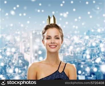 people, holidays, royalty and christmas concept - smiling woman in evening dress wearing golden crown over snowy city background