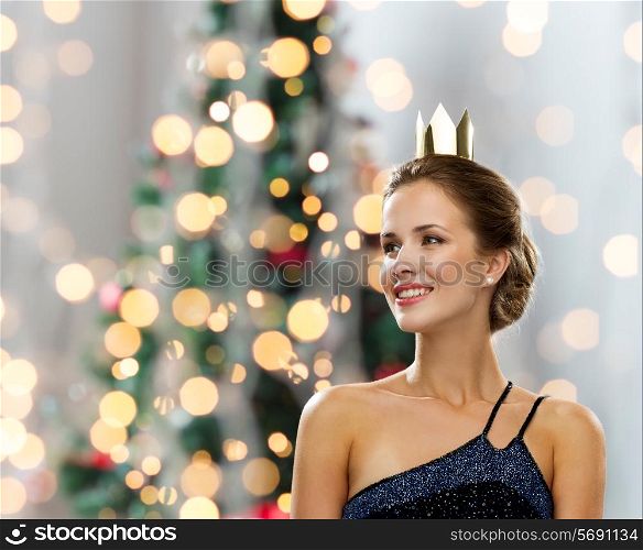 people, holidays, royalty and glamour concept - smiling woman in evening dress wearing golden crown over christmas tree lights background