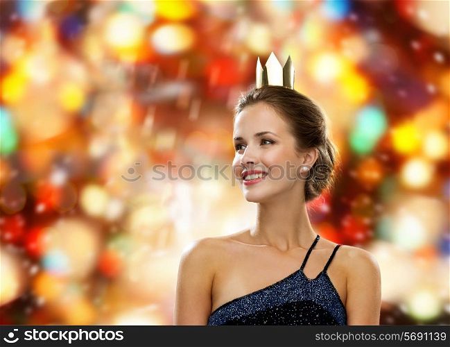people, holidays, royalty and glamour concept - smiling woman in evening dress wearing golden crown over red lights background