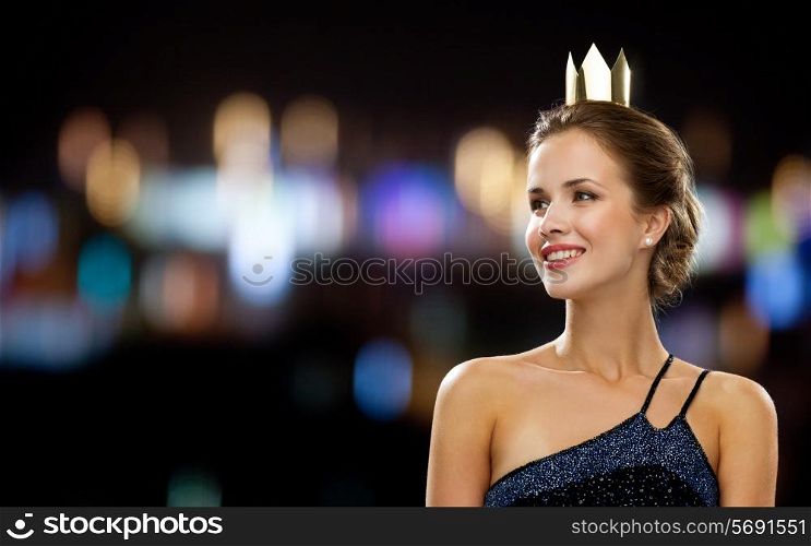 people, holidays, royalty and glamour concept - smiling woman in evening dress wearing golden crown over night lights background