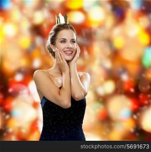 people, holidays, royalty and glamour concept - smiling woman in evening dress wearing golden crown over red lights background