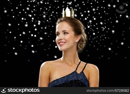 people, holidays, royalty and glamour concept - smiling woman in evening dress wearing golden crown over black snowy background