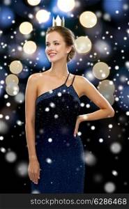 people, holidays, royalty and glamour concept - smiling woman in evening dress wearing golden crown over night lights and snow background