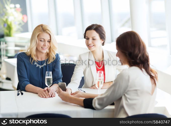 people, holidays, technology and lifestyle concept - happy women with smartphone drinking champagne at restaurant