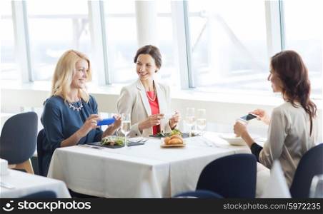 people, holidays, technology and lifestyle concept - happy women with smartphones taking picture of food at restaurant