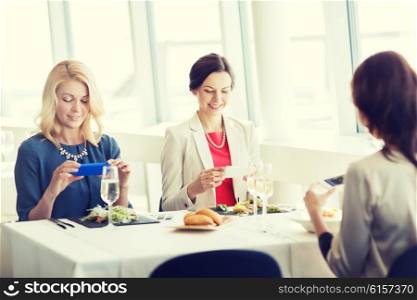 people, holidays, technology and lifestyle concept - happy women with smartphones taking picture of food at restaurant