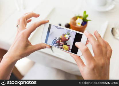 people, holidays, technology, food and lifestyle concept - close up of woman with smartphone taking picture of dessert at restaurant