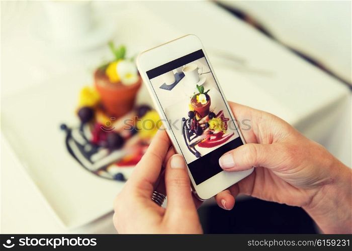people, holidays, technology, food and lifestyle concept - close up of woman with smartphone taking picture of dessert at restaurant