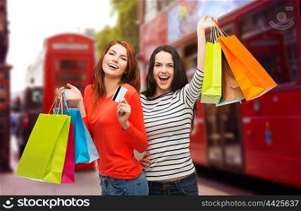 people, holidays, tourism, travel and sale concept - two smiling teenage girls with shopping bags and credit card over london city street background