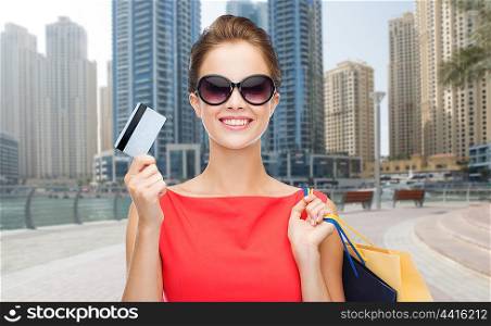people, holidays, tourism, travel and sale concept - young happy woman with shopping bags and credit card over dubai city street background