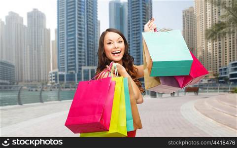 people, holidays, tourism, travel and sale concept - young happy woman with shopping bags over dubai city street background