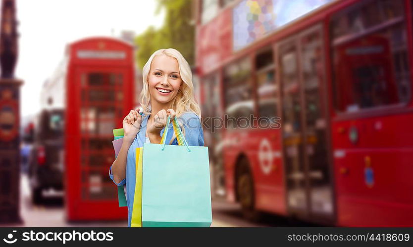 people, holidays, tourism, travel and sale concept - young happy woman with shopping bags over london city street background