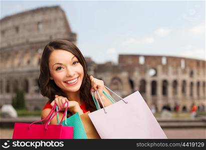 people, holidays, tourism, travel and sale concept - young happy woman with shopping bags over coliseum background