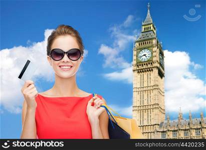 people, holidays, tourism, travel and sale concept - young happy woman with shopping bags and credit card over big ben clock tower background
