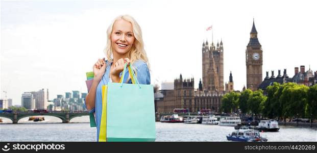 people, holidays, tourism, travel and sale concept - young happy woman with shopping bags over london city background