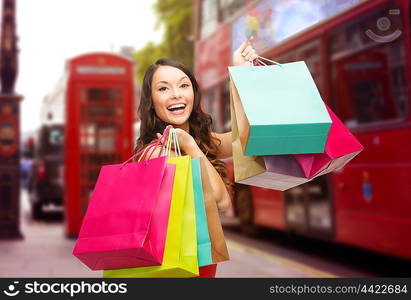 people, holidays, tourism, travel and sale concept - young happy woman with shopping bags over london city street background