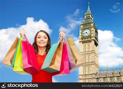 people, holidays, tourism, travel and sale concept - young happy woman with shopping bags over big ben clock tower background