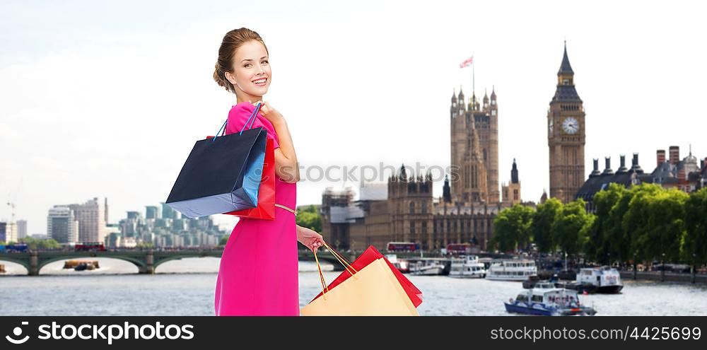 people, holidays, tourism, travel and sale concept - young happy woman with shopping bags over london city background