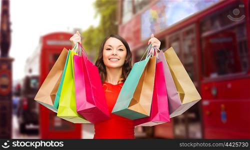 people, holidays, tourism, travel and sale concept - young happy woman with shopping bags over london city street background