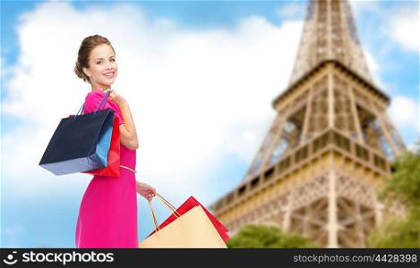 people, holidays, tourism, travel and sale concept - young happy woman with shopping bags over paris eiffel tower background