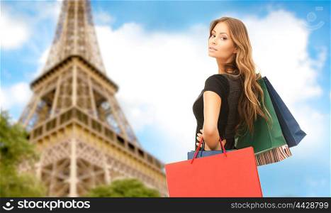 people, holidays, tourism, travel and sale concept - young happy woman with shopping bags over paris eiffel tower background