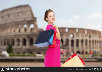 people, holidays, tourism, travel and sale concept - young happy woman with shopping bags over coliseum background