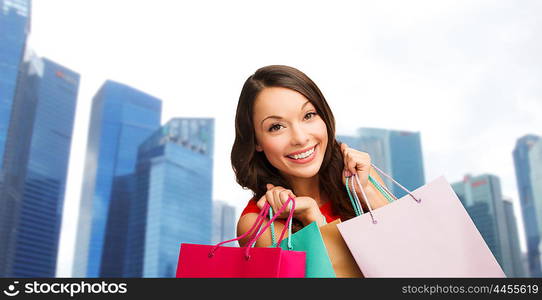 people, holidays, tourism, travel and sale concept - young happy woman with shopping bags over singapore city skyscrapers background