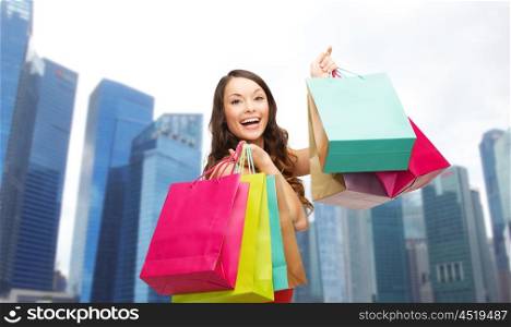 people, holidays, tourism, travel and sale concept - young happy woman with shopping bags over singapore city skyscrapers background