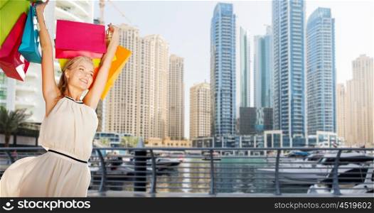 people, holidays, tourism, travel and sale concept - young happy woman with shopping bags over dubai city skyscrapers background