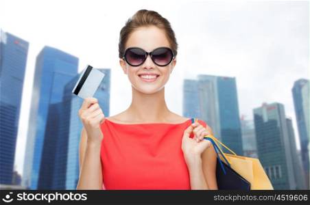 people, holidays, tourism, travel and sale concept - young happy woman with shopping bags and credit card over singapore city skyscrapers background