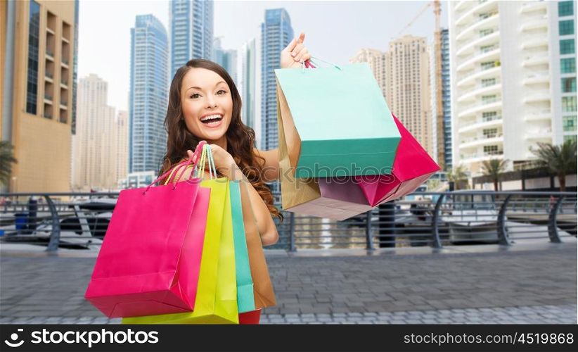 people, holidays, tourism, travel and sale concept - young happy woman with shopping bags over dubai city skyscrapers background