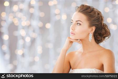 people, holidays, wedding, jewelry and luxury concept - beautiful woman wearing shiny diamond earrings over lights background