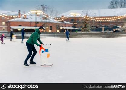 People, holidays, winter, leisure concept. Happy bearded male skater spends Saturday on skating ring, practices and learns new tricks, entertains himself, being in good festive mood.