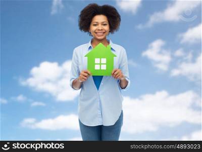 people, home and real estate concept - happy african american young woman with green house icon over blue sky and clouds background