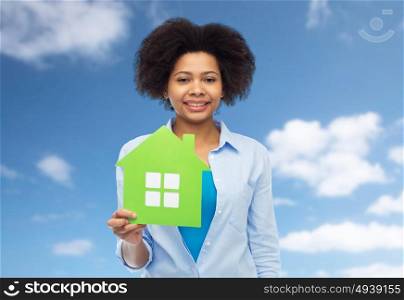 people, home and real estate concept - happy african american young woman with green house icon over blue sky and clouds background. happy african american woman with green house icon