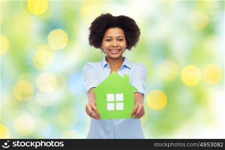 people, home and real estate concept - happy african american young woman with green house icon over summer green lights background. happy african american woman with green house icon