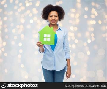 people, home and real estate concept - happy african american young woman with green house icon over lights background. happy african american woman with green house icon