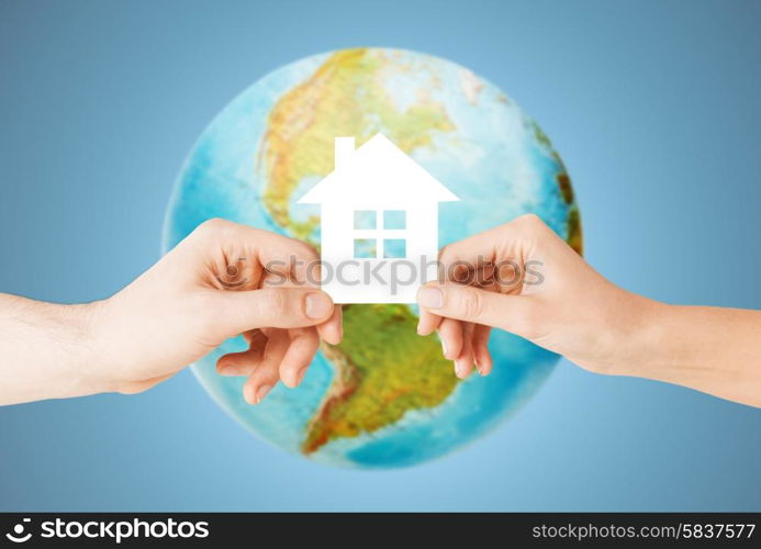 people, home, ecology and land resources saving concept - closeup of woman and man hands holding green paper house over earth globe and blue background