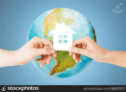 people, home, ecology and land resources saving concept - closeup of woman and man hands holding green paper house over earth globe and blue background