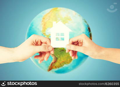 people, home, ecology and land resources saving concept - closeup of woman and man hands holding green paper house over earth globe and blue background