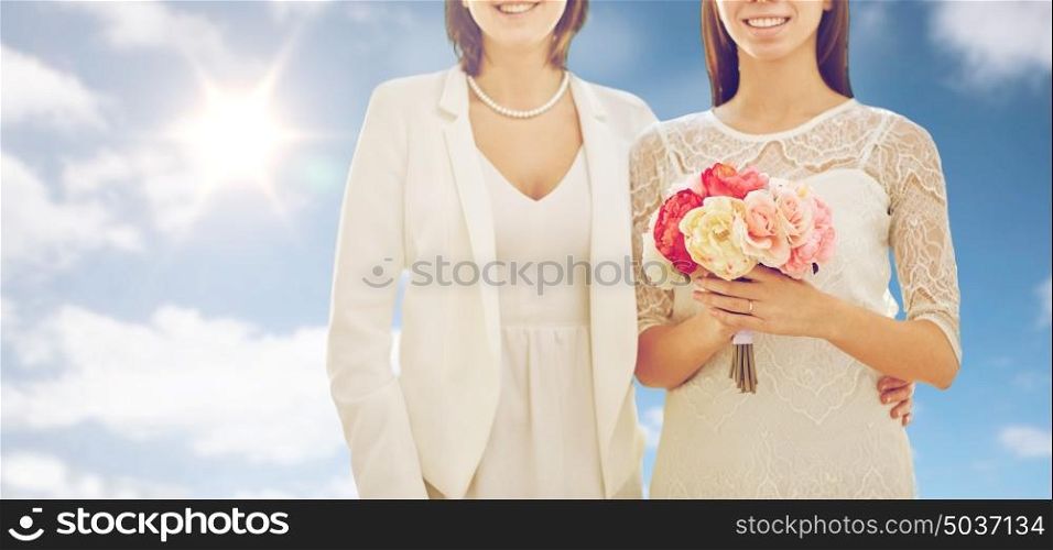 people, homosexuality, same-sex marriage and love concept - close up of happy married lesbian couple with flower bunch over sky and sun background. close up of happy lesbian couple with flowers