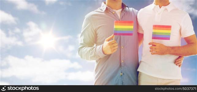 people, homosexuality, same-sex marriage and love concept - close up of happy male gay couple hugging and holding rainbow flags over sky and sun background. close up of male gay couple holding rainbow flags