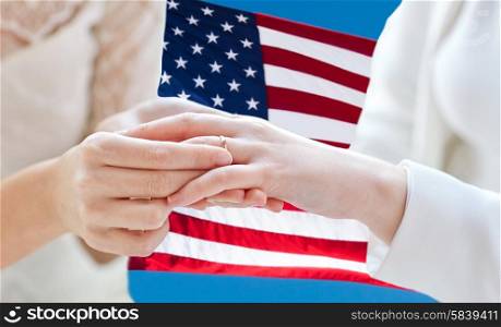 people, homosexuality, same-sex marriage and love concept - close up of happy lesbian couple hands putting on wedding ring over american flag background