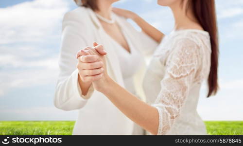 people, homosexuality, same-sex marriage and love concept - close up of happy married lesbian couple dancing over blue sky and grass background
