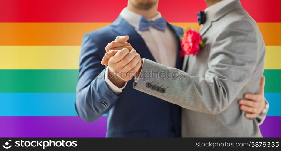 people, homosexuality, same-sex marriage and love concept - close up of happy male gay couple holding hands and dancing on wedding over rainbow flag background