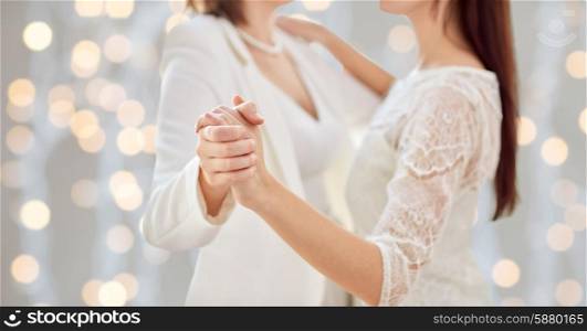 people, homosexuality, same-sex marriage and love concept - close up of happy married lesbian couple dancing over holiday lights background
